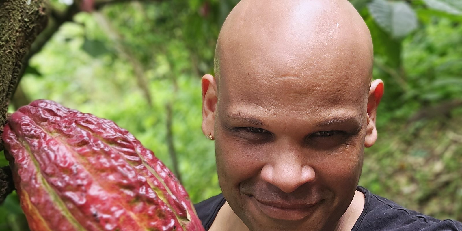 Kenny Santana hält eine reife rote Kakaofrucht auf der Plantage in der Dominikanischen Republik